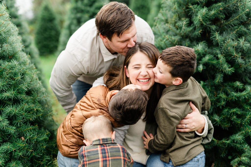 Family enjoying a joyful hug among Christmas trees at a tree farm, capturing holiday spirit, family bonding, and festive celebrations.